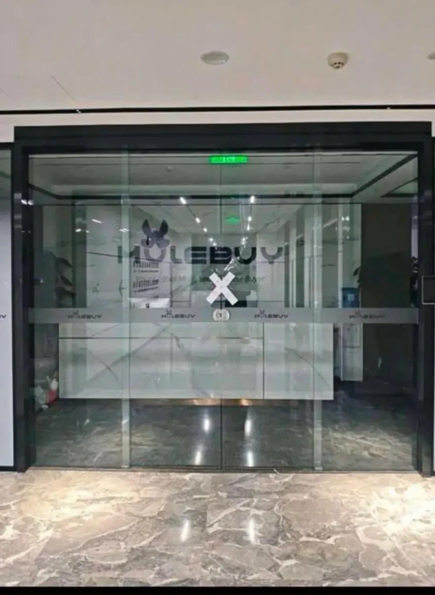 Glass entrance of a Mulebuy-branded office with white X-shaped paper seal strips crossed over the doors